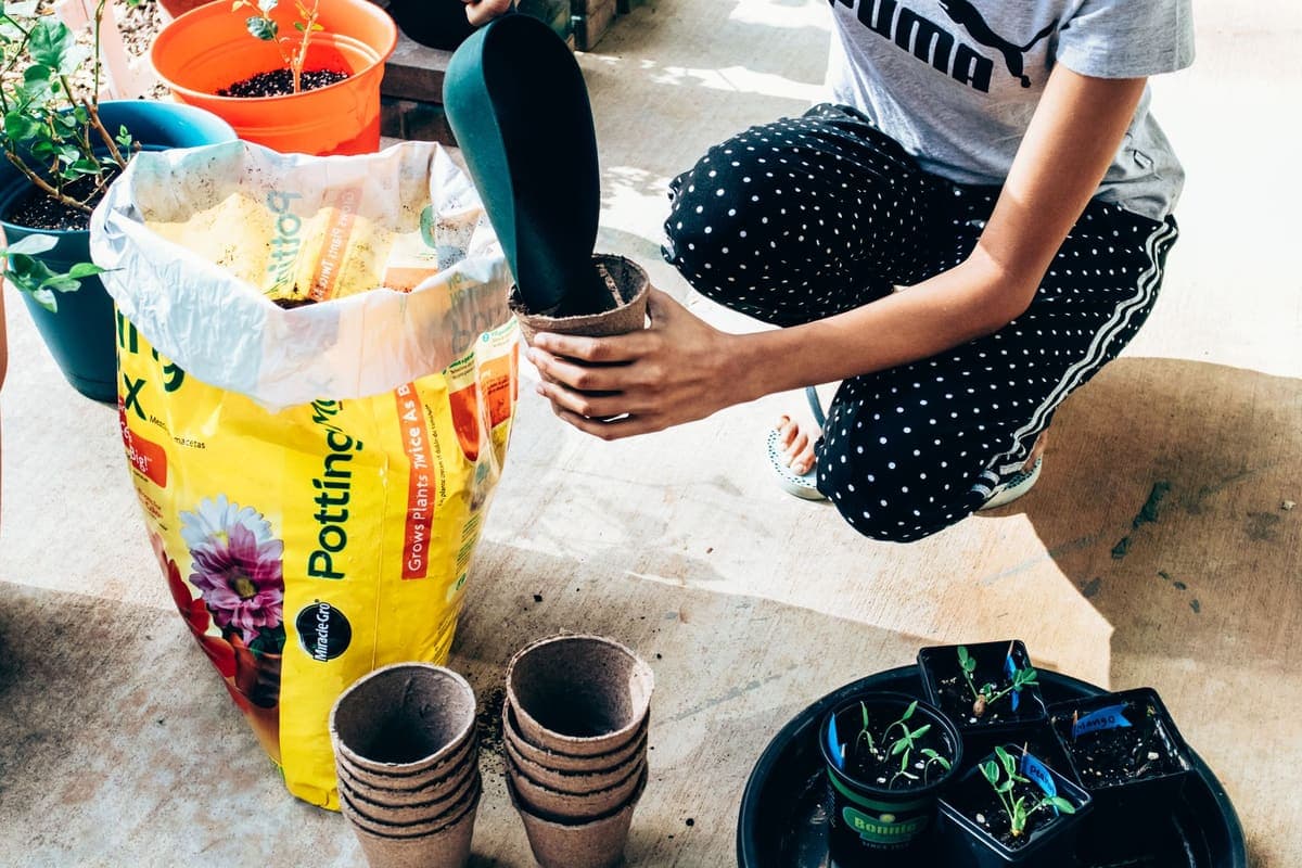 A person kneeling beside an open bag of potting soil with empty pots