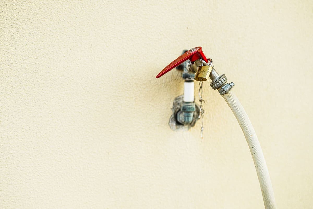 An outdoor tap with a red handle and a garden hose attached