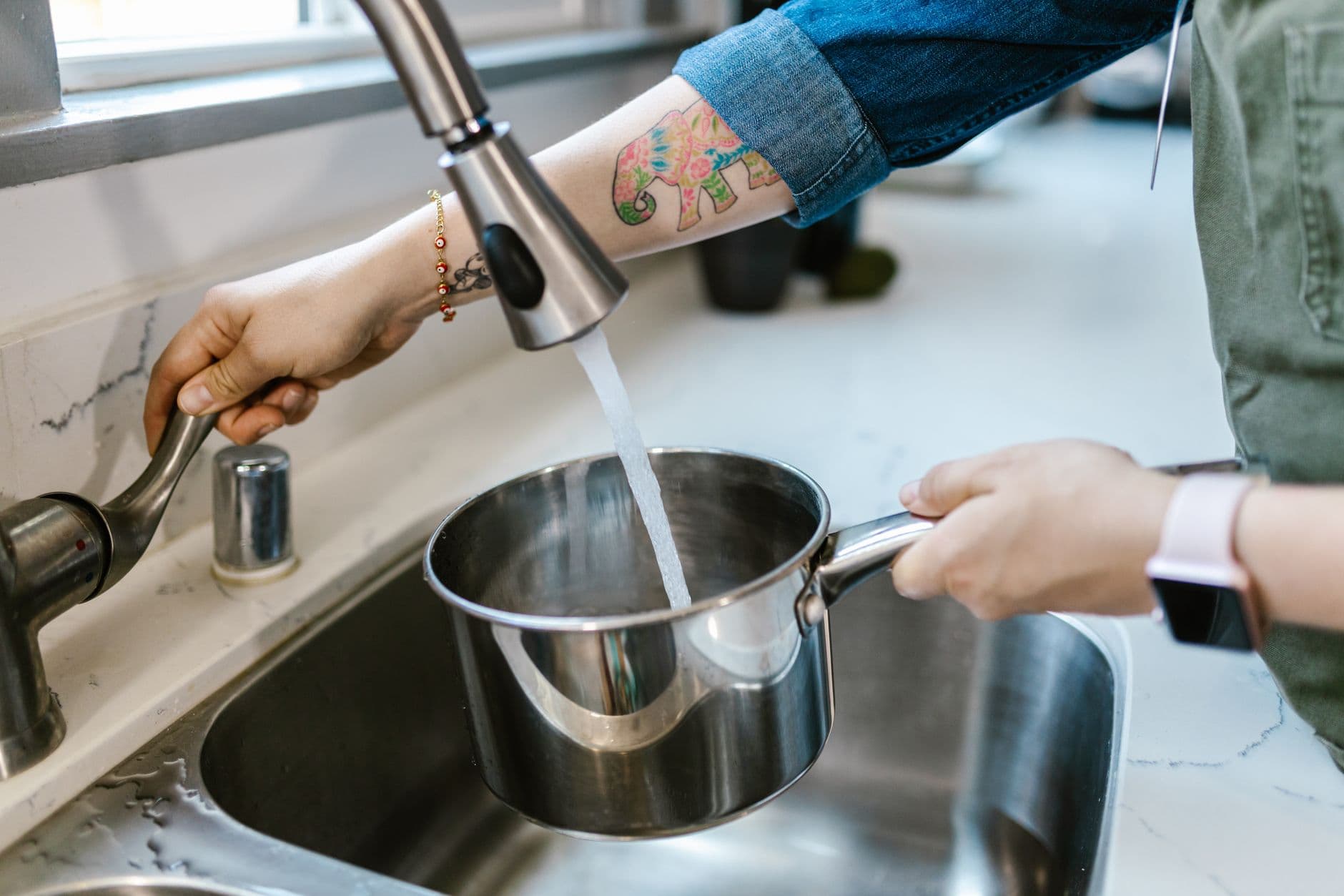 Hands filling a pot with tap water at a kitchen sink