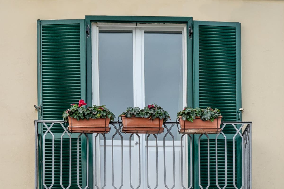 Flower boxes on a balcony railing beneath green shutters